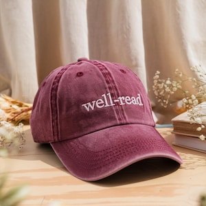 May include: A burgundy baseball cap with the text "well-read" embroidered in white on the front.
