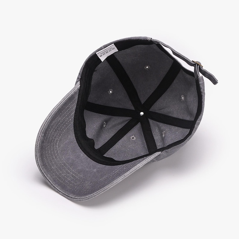 May include: A gray baseball cap with a curved brim, viewed from the inside. The cap has a distressed look, with a black interior and a strap for adjustment. The cap is made of a soft material.