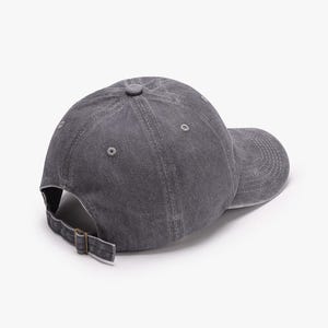 May include: A gray baseball cap with a curved brim and adjustable strap. The cap is made of a textured fabric and features a small button on top. The back of the cap has a metal buckle for adjustment.