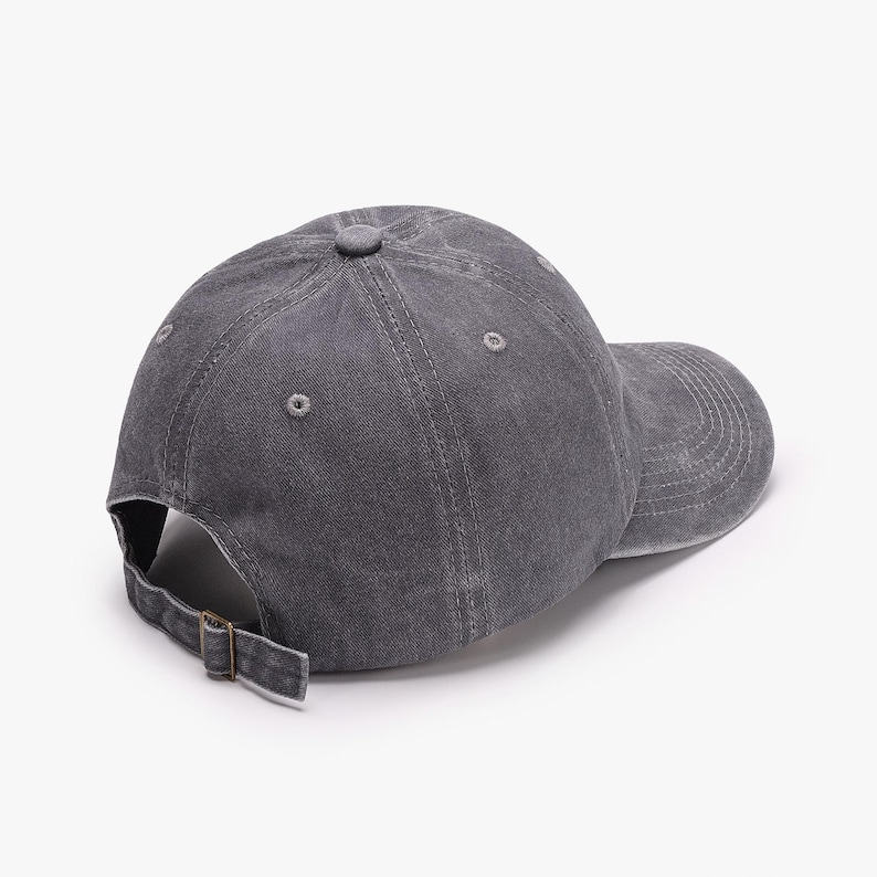 May include: A gray baseball cap with a curved brim and adjustable strap. The cap is made of a textured fabric and features a small button on top. The back of the cap has a metal buckle for adjustment.