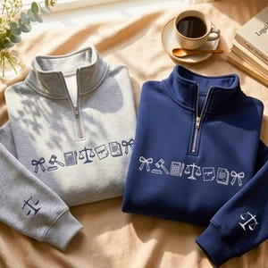 Puede incluir: Dos sudaderas con cremallera de cuarto de cremallera, una gris y otra azul marino, con dibujos lineales blancos de símbolos legales. La sudadera gris tiene una manga gris a juego con una balanza de la justicia.