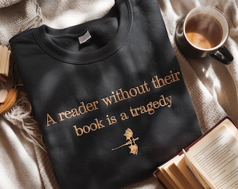 May include: A black sweatshirt with a gold embroidered quote: "A reader without their book is a tragedy". A small gold dragon design is below the quote.