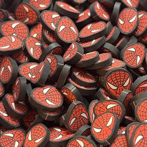 May include: A collection of small, circular, flat discs featuring a red and black webbed pattern with white eye shapes, resembling the mask of a superhero. Each disc has a black edge and a consistent graphic design printed on the top surface.