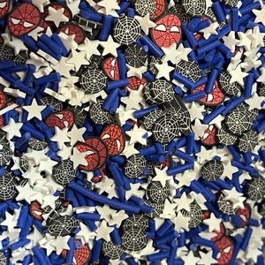 May include: A colorful assortment of polymer clay sprinkles featuring a mix of shapes and designs. The mix includes white star shapes, blue rod shapes, and circular designs with a spider web and Spider-Man's face.