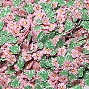 May include: A large pile of pink and green resin flower and cactus charms. The flowers have a white center and the cacti have a green and white striped pattern.