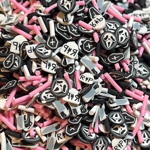 May include: A close-up shot of a pile of polymer clay pieces in various shapes and colors. The pieces include pink rods, black and white coffin shapes, gray knives, and white pieces with the text "RIP" and "949".