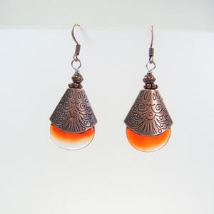 May include: A pair of copper earrings with a teardrop-shaped orange glass bead and an intricate copper design.