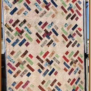 May include: A colorful quilt with a geometric pattern of squares and rectangles. The quilt is made with a variety of fabrics in shades of red, blue, green, and brown. The quilt is quilted with a swirling pattern. The quilt is titled "Spin Cycle".