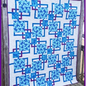 Puede incluir: Un edredón blanco con un diseño geométrico con cuadrados y líneas azules y moradas. El edredón tiene un patrón repetitivo de cuadrados llenos de un estampado floral azul. Los textos "Wild Daisy Quilts" y "Circuits" son visibles.