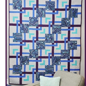 Puede incluir: Una colcha con un patrón geométrico de cuadrados y rectángulos azules, verde azulado y morados sobre un fondo blanco. La colcha se titula "Pathways" y está hecha por Wild Daisy Quilts.