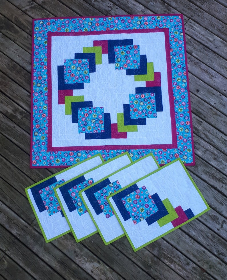 Pu&ograve; includere: Set di cinque tovagliette all'americana con un design geometrico che presenta quadrati in tonalit&agrave; di blu, verde e rosa. Le tovagliette hanno uno sfondo bianco e sono bordate di verde.