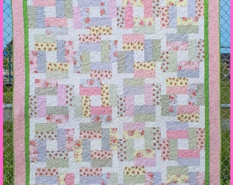 May include: A patchwork quilt with a floral pattern in shades of pink, green, and white. The quilt is framed with a pink and green border. The quilt is labeled "Sunday".