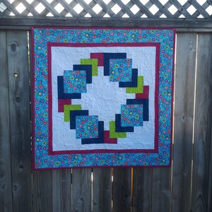 Pu&ograve; includere: Una trapunta colorata con un design geometrico che presenta quadrati in tonalit&agrave; di blu, verde e rosso. La trapunta &egrave; incorniciata da un tessuto floreale blu e rosa.