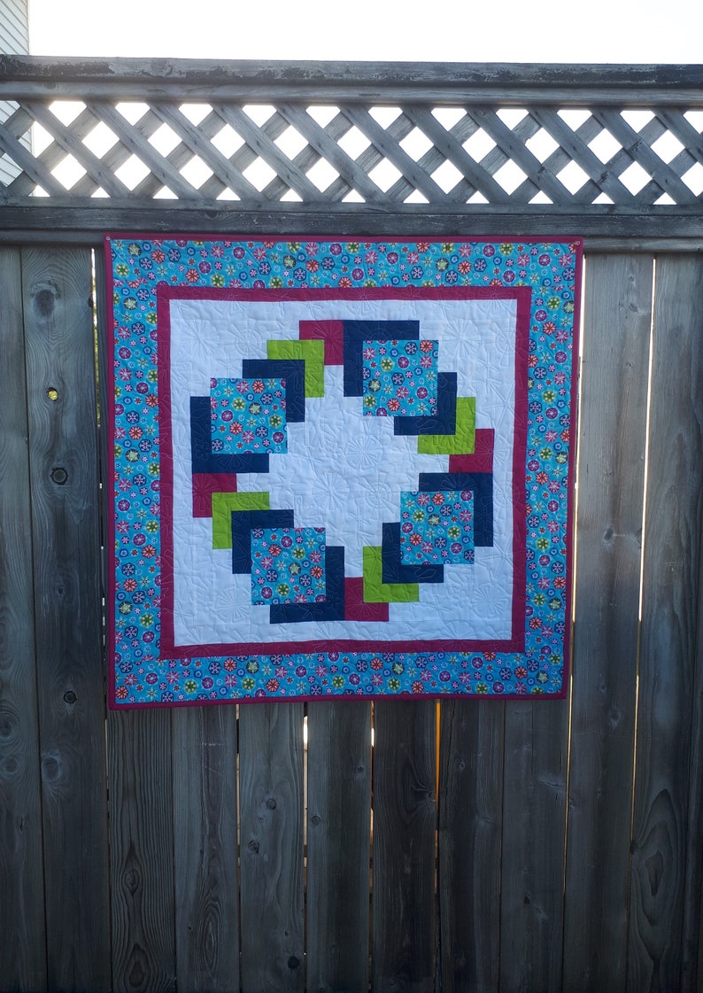 Pu&ograve; includere: Una trapunta colorata con un design geometrico che presenta quadrati in tonalit&agrave; di blu, verde e rosso. La trapunta &egrave; incorniciata da un tessuto floreale blu e rosa.