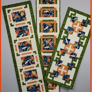 Peut inclure: Trois chemins de table rectangulaires avec des motifs floraux et d'oiseaux. Les chemins de table présentent un fond crème avec des accents verts et orange. Le motif floral comprend des fleurs bleues, oranges et jaunes. Le texte "Table Runner Trio" est en bas.