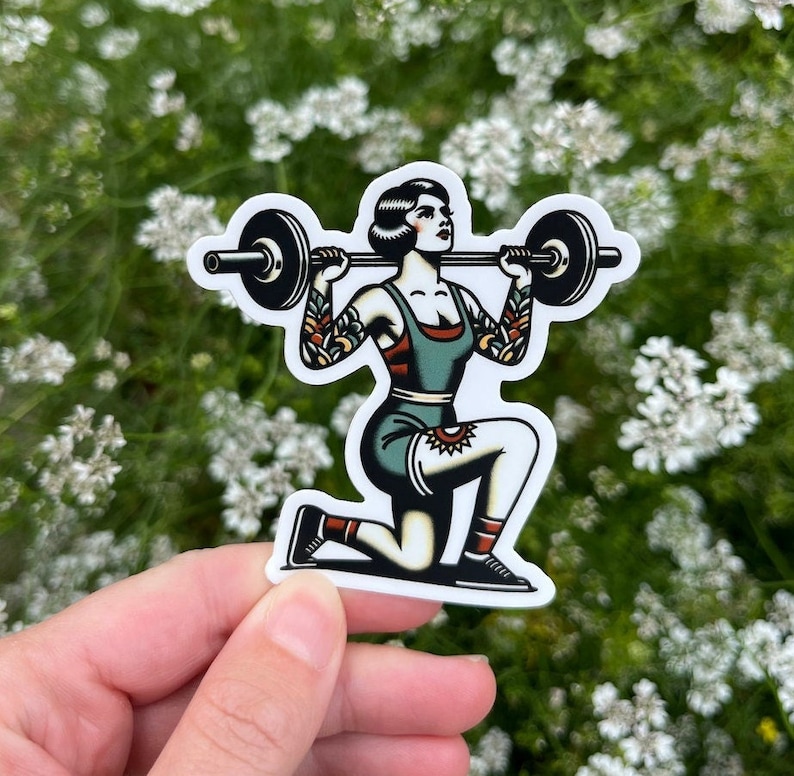 May include: A sticker featuring a vintage-style illustration of a woman lifting a barbell. She is wearing a green and red outfit and has a tattoo on her leg. The sticker is on a white background.
