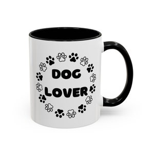 May include: White ceramic mug with a black rim and handle. The mug has a black paw print design with the text "DOG LOVER" in the center.