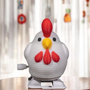 May include: A white wind-up toy chicken with red and yellow accents. The chicken has a red comb and wattle, yellow beak, and black eyes.