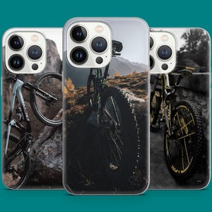 May include: Three phone cases with a mountain biking design. The cases are clear and show a black mountain bike with a white frame and black wheels. The background is a blurry image of a mountain.