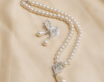May include: A pearl necklace and matching earrings set. The necklace features two strands of round pearls with a decorative silver pendant and a pear-shaped pearl drop. The earrings have a similar design with a pearl drop.