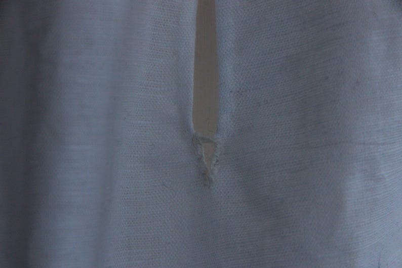 May include: A white fabric garment featuring a vertical slit opening at the neckline. The material has a visible woven texture with a slightly translucent quality. The edges of the slit are finished with stitching, showing a small triangular reinforcement.