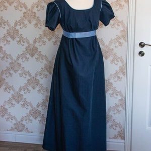 May include: A floor-length dark navy blue dress featuring short puff sleeves, a square neckline with light blue piping, and a wide light blue ribbon sash positioned at the empire waistline. The garment is displayed on a mannequin form.