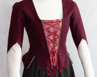 May include: A deep burgundy bodice featuring a central panel with a red and gold floral brocade pattern, secured by a red ribbon lace-up closure. The garment has three-quarter length sleeves with open cuffs, revealing white undersleeves beneath.