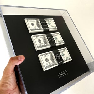 Cornice quadrata trasparente con pile di dollari. Arte del denaro per il successo e la motivazione. Soldi in cornice chiara. Decorazione murale elegante.