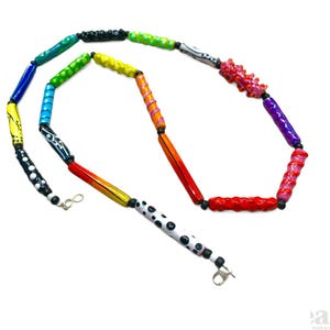 May include: A colorful necklace made of hand-painted glass beads. The beads are arranged in a rainbow pattern, with each bead featuring a unique design. The necklace is finished with silver clasps.