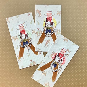 May include: Three rectangular cards featuring a cowboy illustration. The cowboy wears a white hat, red bandana, and brown pants, holding a rope. The background is a light color with a pattern of horses and cacti.