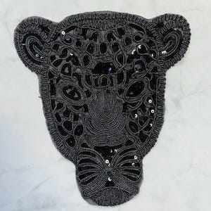 Puede incluir: Aplique de cabeza de jaguar de lentejuelas negras. El aplique está hecho de lentejuelas y cuentas negras y tiene la forma de una cabeza de jaguar. Es perfecto para agregar un toque de glamour a cualquier proyecto.