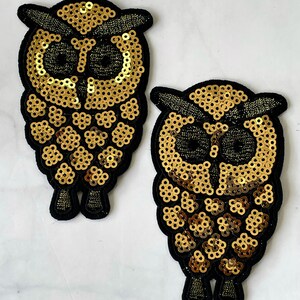May include: Two gold sequined owl patches with black felt backing. The owls have black eyes and beaks.