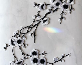 May include: White embroidered floral applique with black outlines. The design features a branch with several blossoms and buds. This applique is perfect for adding a touch of elegance to clothing, bags, or home decor.
