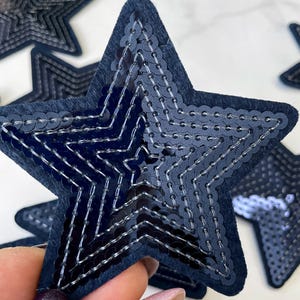 Op de afbeelding: Vijf marineblauwe viltsterren met pailletten. De pailletten zijn in een concentrisch patroon gerangschikt, waardoor een stervorm ontstaat binnen de grotere ster.