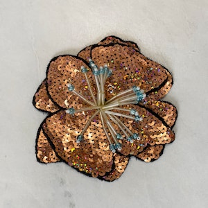 Puede incluir: Una gran flor de lentejuelas marrones con un centro hecho de cuentas de plástico transparente y alambre plateado.