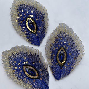 May include: Three blue and gold peacock feather-shaped fabric appliques with sequins.