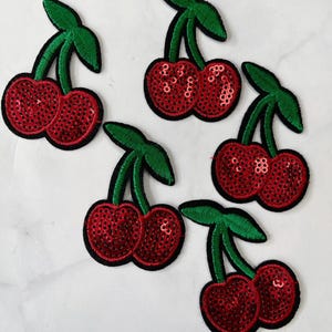 May include: Five red and green cherry patches with sequins. The cherries are embroidered with black thread and have a shiny finish.