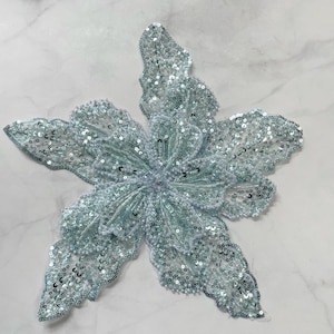 May include: A light blue sequined flower applique with a beaded center. The applique is perfect for adding a touch of sparkle to clothing, bags, or home decor.