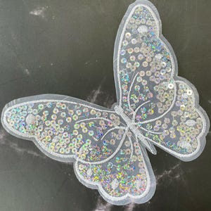 May include: A white iridescent butterfly applique with sequins. This is a great embellishment for clothing, bags, or home decor projects.
