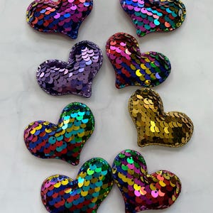May include: Seven iridescent heart-shaped sequins in various colors, including purple, gold, and rainbow.