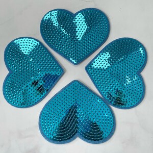 Könnte beinhalten: Vier blaue Pailletten-Herzen. Jedes Herz besteht aus blauen Pailletten auf einem Filz-Untergrund.