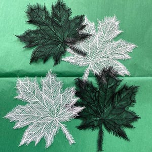 Pode incluir: Quatro folhas de bordo de renda, duas pretas e duas brancas, sobre um fundo verde.