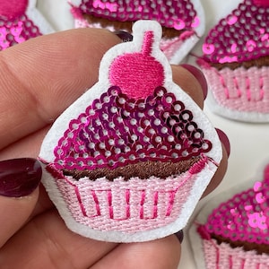 May include: Pink and brown cupcake-shaped felt applique with pink sequins and a pink cherry on top.