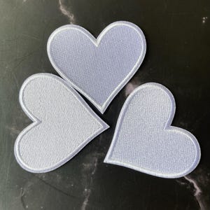 May include: Three white felt heart-shaped patches with a white outline.