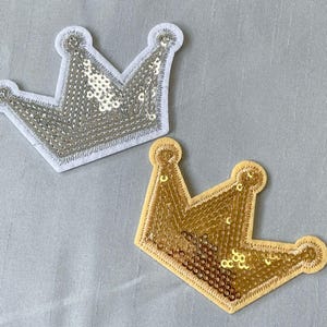 May include: Two felt crown patches, one silver and one gold, with sequins. The crowns are both approximately 7.5 cm wide.