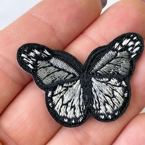 May include: A black and silver embroidered butterfly patch. The butterfly has a detailed design with silver thread outlining the wings.