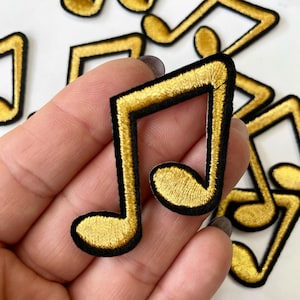 Puede incluir: Parches de hierro en forma de nota musical dorada con contornos negros. Los parches miden aproximadamente 5 cm de alto.