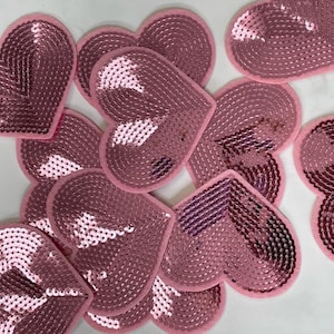 Puede incluir: Un grupo de lentejuelas de color rosa en forma de corazón, cada una con un diseño diferente. Las lentejuelas están dispuestas en una pila, con algunas superpuestas.