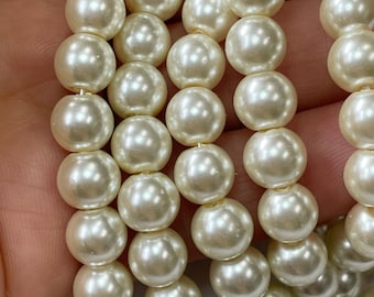 May include: A strand of off-white pearl beads. The beads are round and smooth, and they have a slight iridescent sheen.