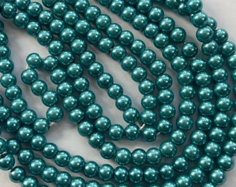 May include: A strand of teal green pearl beads. The beads are round and have a metallic sheen.